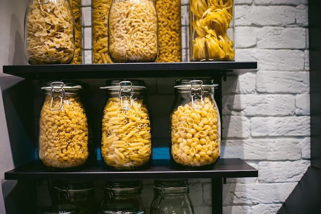 Photo close-up of pasta in jars on shelves in kitchen at home