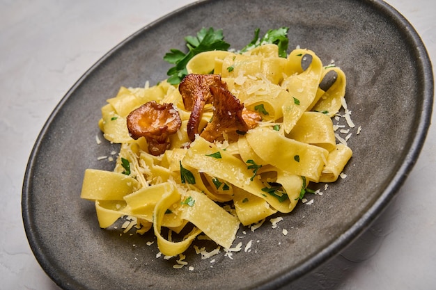 Foto close-up pasta pappardelle met champignons, cantharellen, kaas en peterselie op donkere ovale plaat