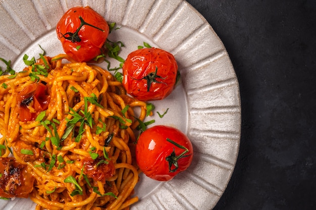 Photo close up pasta with baked cherry tomatoes, cheese and parsley on a dark textured background