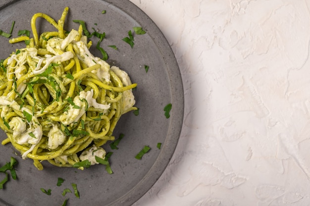 Close up pasta with pesto, stracciatella cheese and parsley served on gray ceramic plate on light