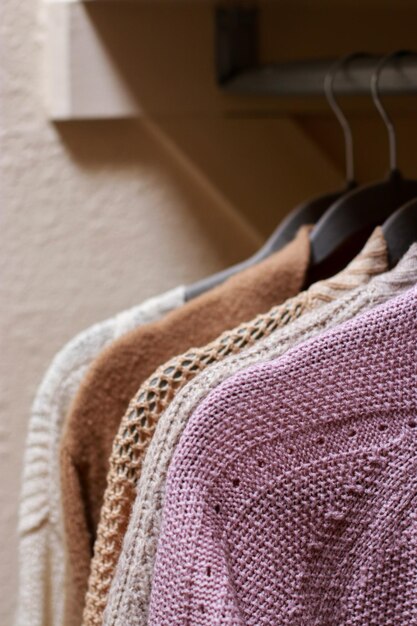 close up of pastel warm knitted cardigan sweater hanging in the closet. Cozy fall and winter wardrob