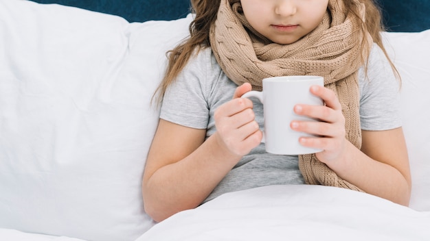 Foto primo piano della ragazza paziente con la sciarpa intorno al suo collo che tiene la tazza da caffè bianca