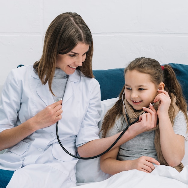 Foto primo piano della ragazza di un paziente che ascolta il battito del cuore di medico femminile sorridente con lo stetoscopio