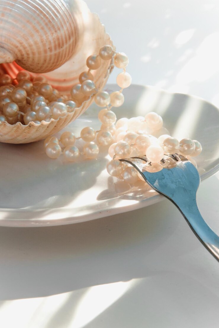 Photo close-up of pearls with seashell and fork in plate on table