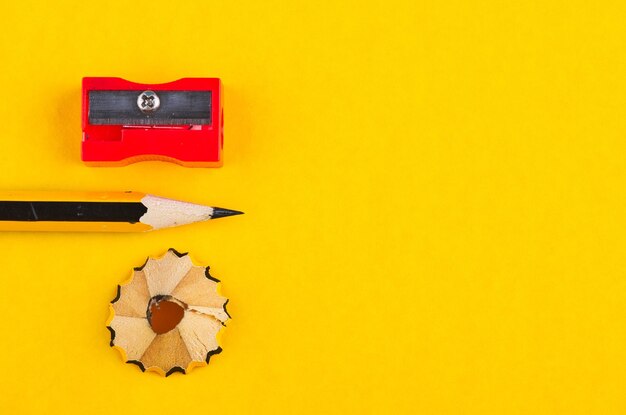 Close-up of pencil by shaving and sharpener against yellow background