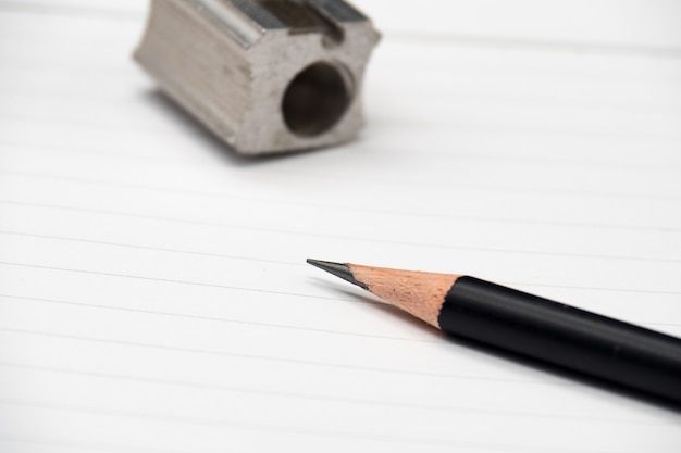 Close up pencil, pencil sharpener and blank notebook on wooden background.