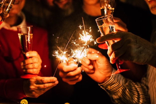 Close up of people celebrate new year eve with sparklers and sparkling wine - nightlife concept - birthday or party friends having fun together