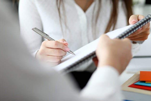 Close-up of people sitting in office and writing something in important document with tender female hands. Smart businessman holding paper folder.