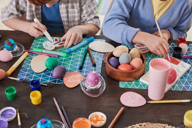 Close-up of people sitting at the table painting eggs with paintbrushes they preparing for Easter together