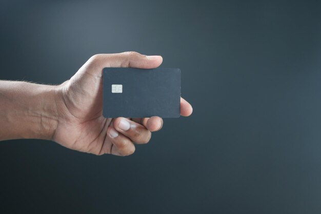 Foto primo piano della mano della persona che tiene la carta di credito su sfondo nero