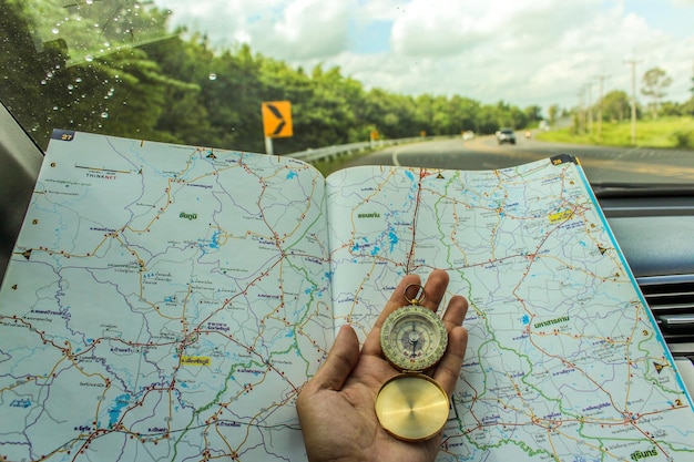 Photo close-up of person hand holding navigational compass with map by car windshield