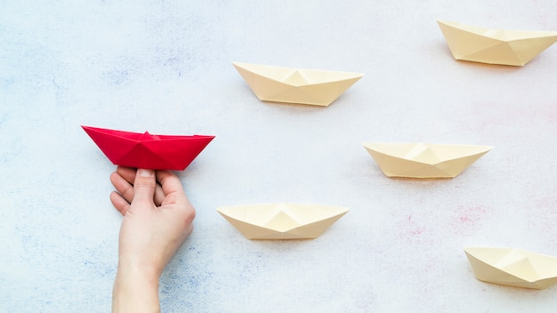 Photo close-up of a person hand holding red boat among the white paper boats on blue textured backdrop