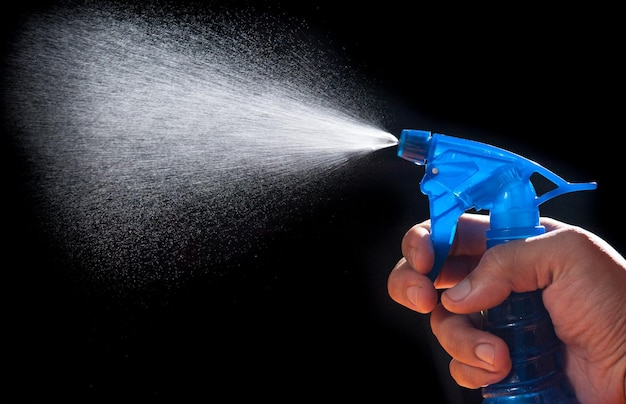 Close-up of person hand holding spray bottle against black background