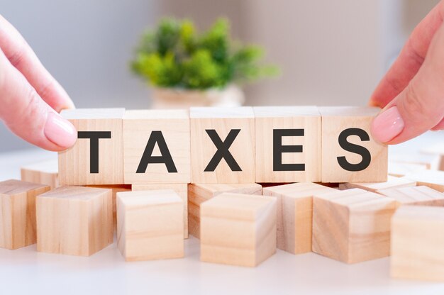 Close-up of person hand holding the word TAXES on wooden table. Business concept. Selective focus.