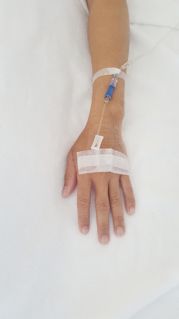 Close-up of person hand with iv drip on bed