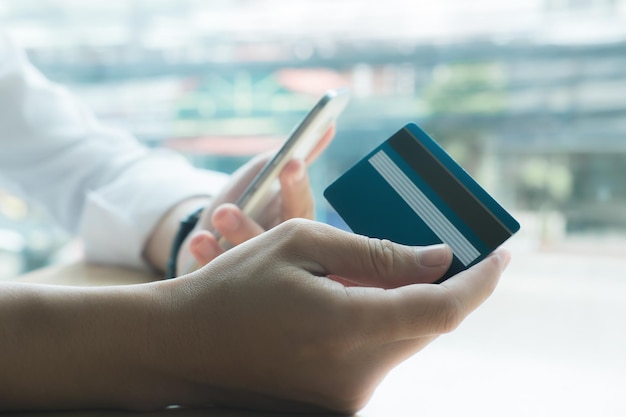 Foto close-up di una persona con una carta di credito mentre usa il telefono cellulare per fare acquisti online
