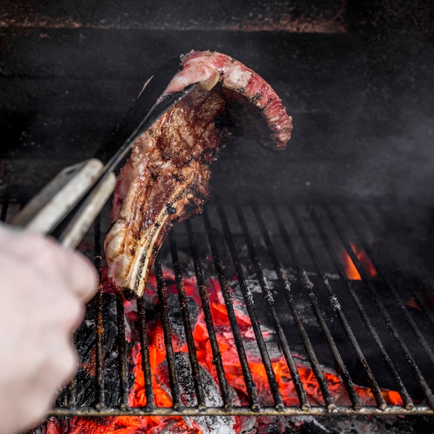 Close-up of a person holding roasted beef with tong on charcoal grilled