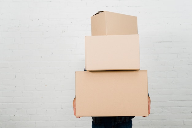 Close-up of a person holding stack of cardboard boxes against white painted wall