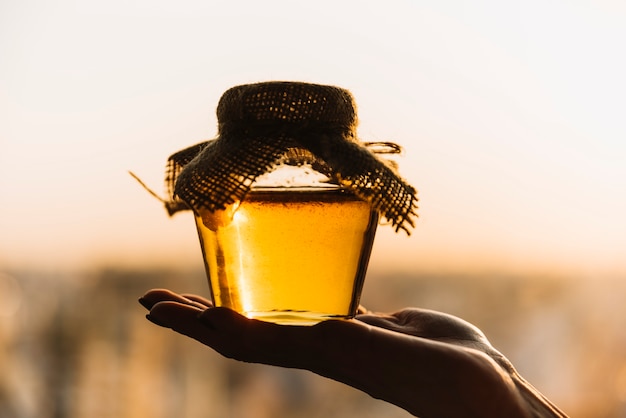 Close-up of a person's hand holding jar of fresh honey