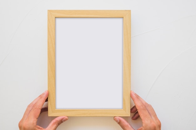 Foto primo piano della mano di una persona che tiene cornice in legno bianco sulla parete