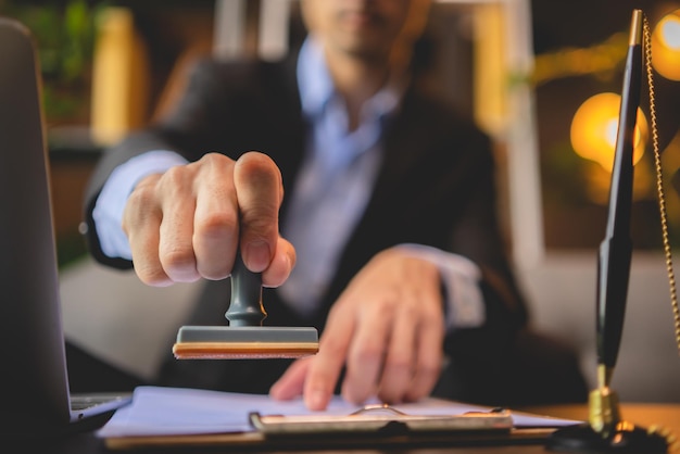 Close-up of a person\'s hand stamping with approved stamp on\
approval certificate document public paper at desk, notary or\
business people work from home, isolated for coronavirus covid-19\
protection