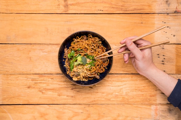 Close-up of a person's picking the noodles with chopsticks on wooden plank