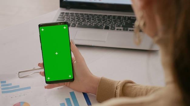 Close up of person with green screen on mobile phone, vertically holding chroma-key on display. Woman looking at isolated template and mock-up background on smartphone. Mockup blank app