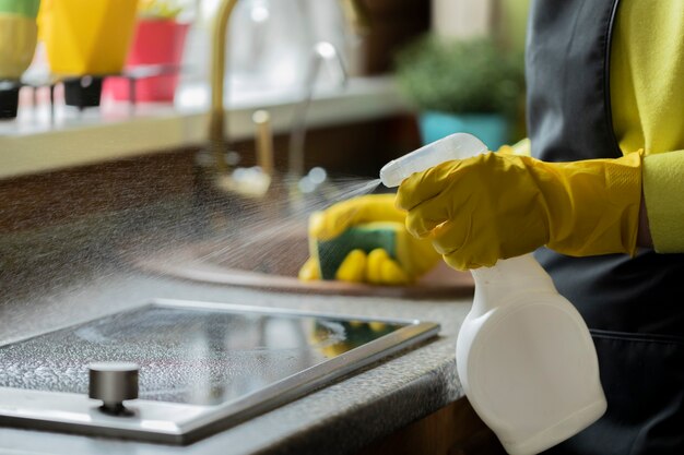 Close up person in yellow rubber gloves cleaning house, wipes kitchen worktop using spray detergent, washes induction stove with sponge