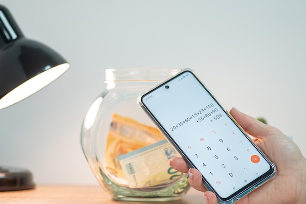 Close up of phone in female hand counting savings Jar with euro money on the background