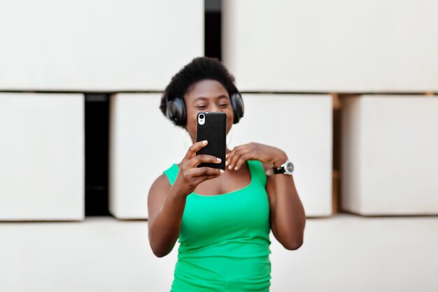 Foto primo piano del telefono nelle mani di una ragazza africana che ascolta musica con le cuffie wireless sul suo telefono cellulare, balla e si fa un selfie.