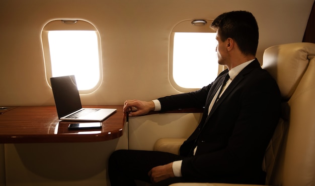 Close-up photo of an attractive man in a suit, who is sitting in profile in his window seat on the plane