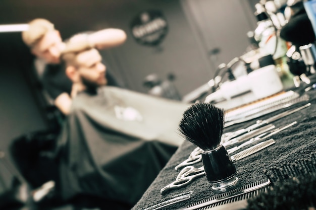 Close up photo of a barber toolkit of a wooden brush, trimmers, and scissors, lying on a barbershop counter.