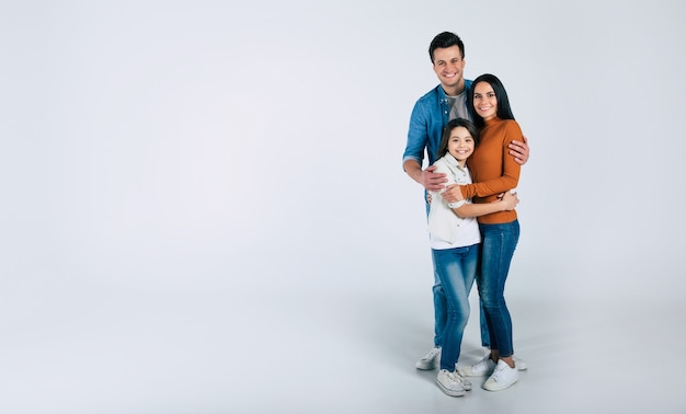 Close-up photo of beautiful family of mother, father and cute little child in between, who are looking in the camera and smiling sincerely.