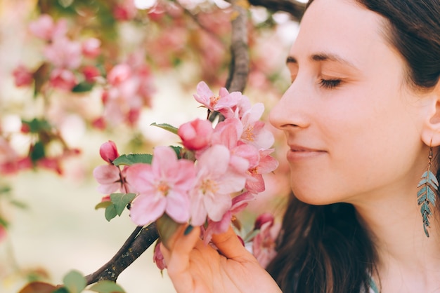 木の上の素敵なピンクの花の匂いを嗅ぐ美しい女性の写真を閉じる