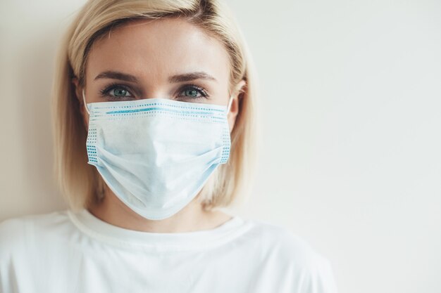 Chiuda sulla foto di una donna caucasica con maschera medica e capelli biondi vicino allo spazio libero bianco