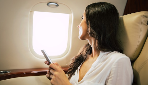 Close-up photo of a charming woman flying business class, who is smiling and looking in the camera while talking on the phone.