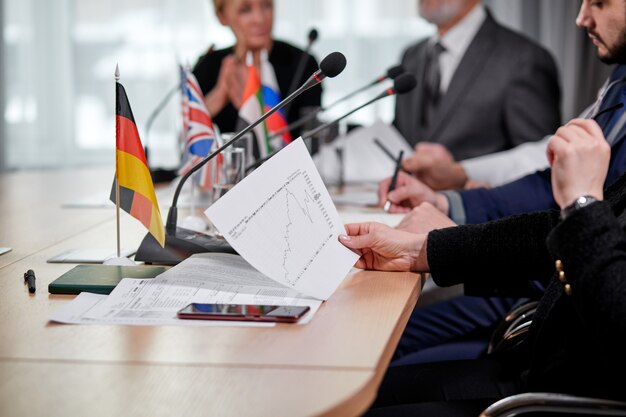 Close-up photo of chart document in hands of female executive during interracial business meeting in modern office, people sitting at desk