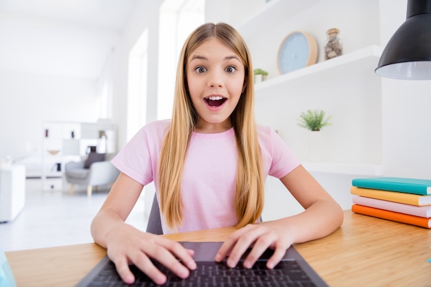 Close up photo of excited little kid girl sit comfort cozy table study remote use laptop video call impressed teacher speak talk good grades exam  typing in house indoors