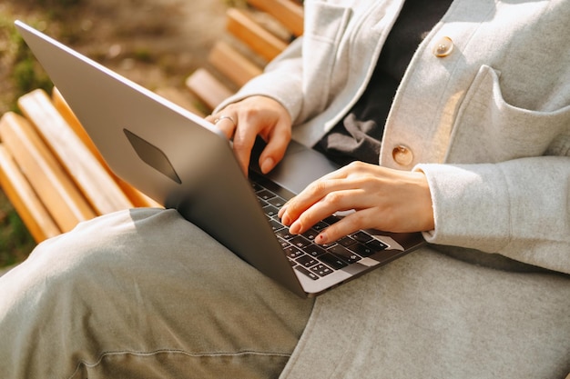 Close up photo of female hands typing on the laptop while sitting on a bench