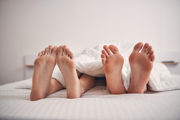 Close up photo of four legs in bed belonging to loving couple