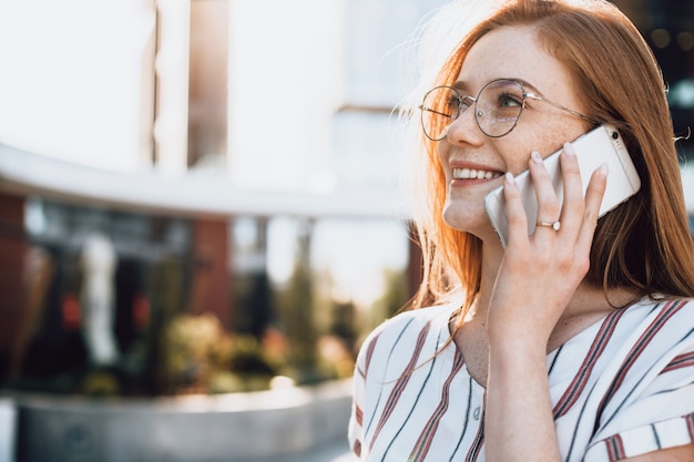 Close up photo of a ginger caucasian business lady with freckles and glasses who is speaking on phone with some clients