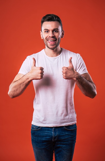 Close up photo of handsome smiling man in t-shirt is showing thumb up and looks on camera