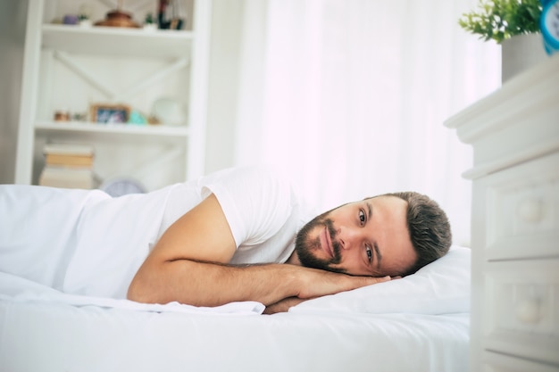 Close up photo of handsome young bearded man lying in bed and relaxing on the morning