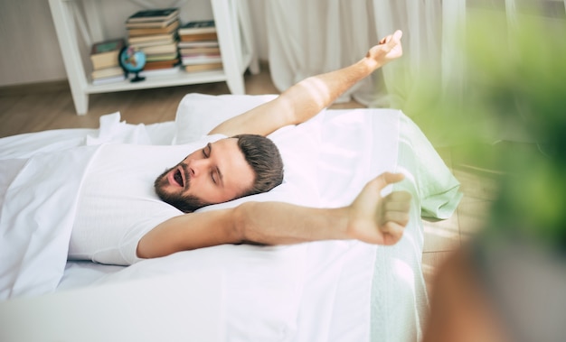 Close up photo of handsome young bearded man lying in bed and relaxing on the morning