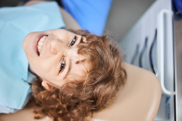 Close-up photo of a happy boy wearing a sanitary napkin around his neck while lying down in dental chair