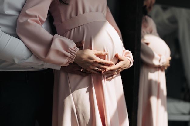 Photo close up photo of happy pregnant woman at home with man holding her belly in white shirt near mirror