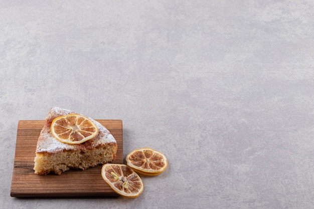 Close up photo of homemade cake slice with dried lemon slices on wooden board. 