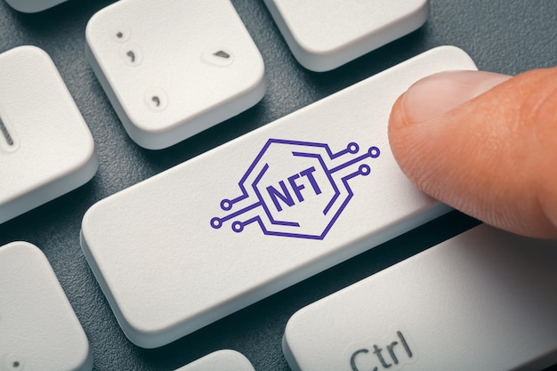 Close-up photo of index finger pressing computer key with NFT symbol. Electronic Non-Fungible Token.