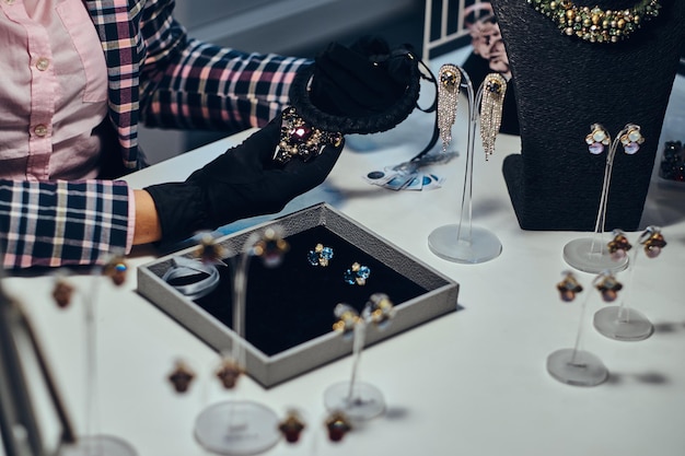 Close-up photo of a jewelry worker presenting a costly necklace with gemstones in a luxury jewelry store.