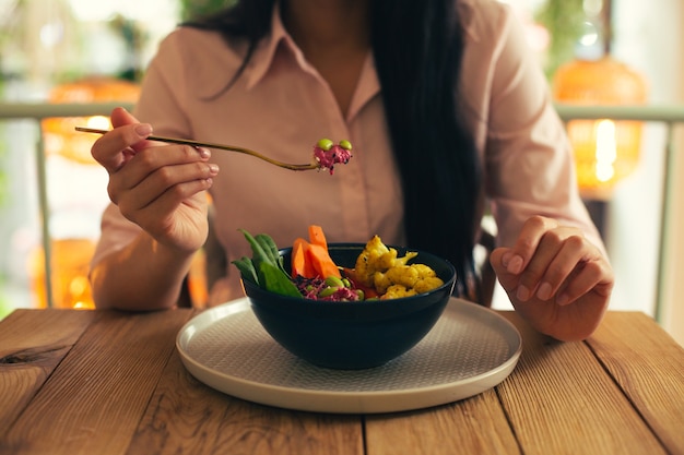 Foto ravvicinata della signora con una camicetta rosa seduta al tavolo e che prende il suo pasto vegetariano su una forchetta